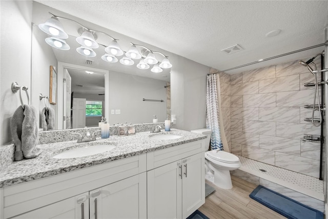 bathroom with a tile shower, toilet, visible vents, and a sink