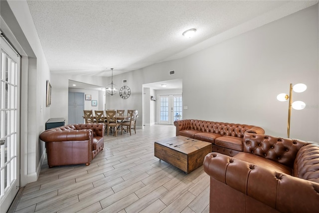 living room featuring a textured ceiling, light wood-type flooring, baseboards, visible vents, and a notable chandelier
