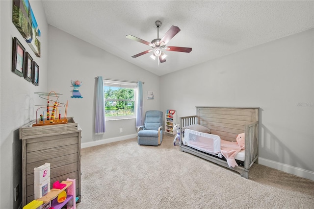 carpeted bedroom featuring a textured ceiling, vaulted ceiling, a ceiling fan, a crib, and baseboards