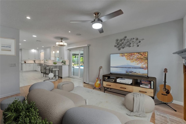 living area featuring light wood-type flooring, a ceiling fan, baseboards, and recessed lighting