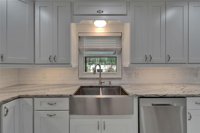 kitchen with stainless steel dishwasher, light stone countertops, decorative backsplash, and a sink