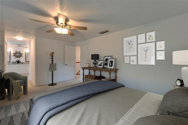 bedroom featuring visible vents, ceiling fan, light colored carpet, a textured ceiling, and ensuite bath
