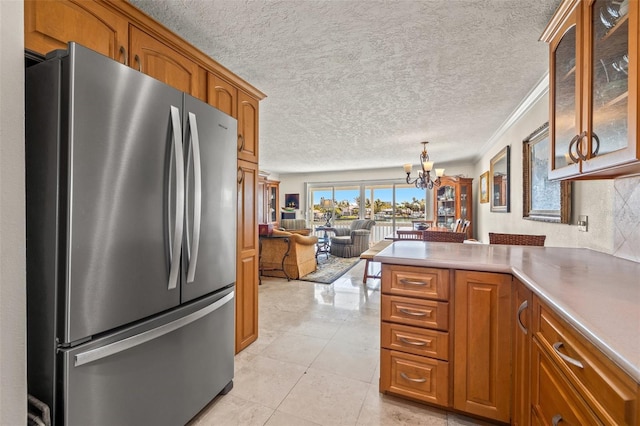 3021 Alton Dr, St Pete Beach, FL 33706 - kitchen featuring freestanding refrigerator, a chandelier, brown cabinetry, a textured ceiling, and ornamental molding