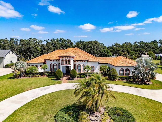 mediterranean / spanish house featuring a tiled roof, curved driveway, and a front yard