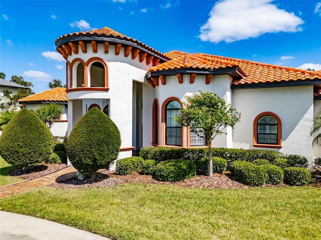 mediterranean / spanish-style home with a tiled roof, stucco siding, and a front lawn