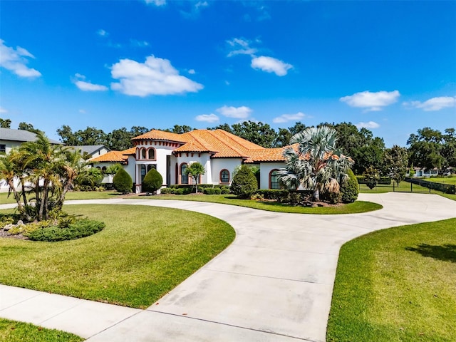 mediterranean / spanish-style house featuring curved driveway, stucco siding, a tile roof, and a front yard