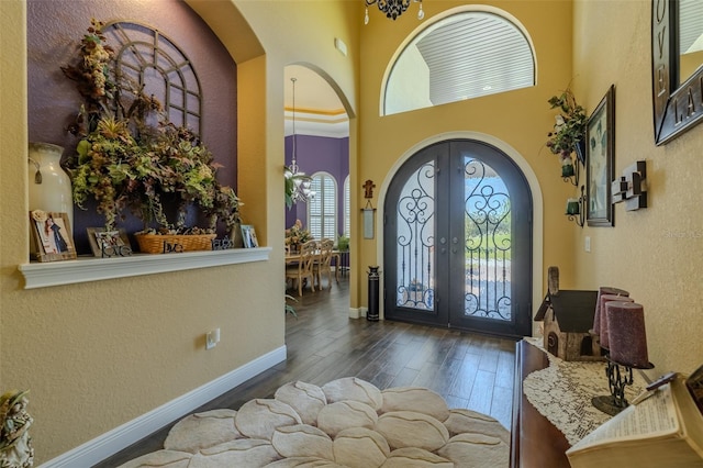 foyer entrance with baseboards, hardwood / wood-style flooring, french doors, arched walkways, and a notable chandelier