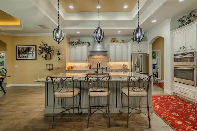 kitchen with a kitchen bar, arched walkways, stainless steel appliances, a tray ceiling, and white cabinetry