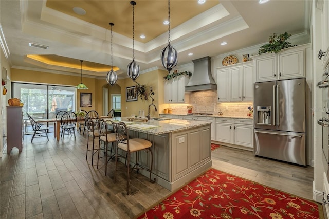 kitchen featuring light wood-style floors, a breakfast bar area, a raised ceiling, custom range hood, and appliances with stainless steel finishes