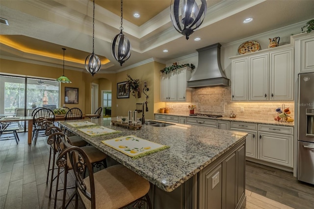 kitchen featuring appliances with stainless steel finishes, a sink, a raised ceiling, custom range hood, and ornamental molding