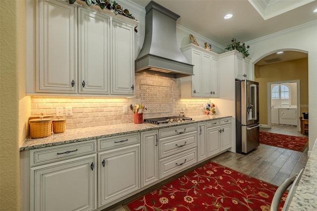 kitchen featuring arched walkways, stainless steel appliances, wood finished floors, custom range hood, and ornamental molding