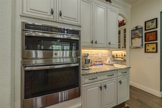 kitchen with crown molding, dark wood-style flooring, stainless steel double oven, baseboards, and tasteful backsplash