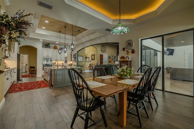 dining area featuring arched walkways, dark wood-style flooring, and a tray ceiling