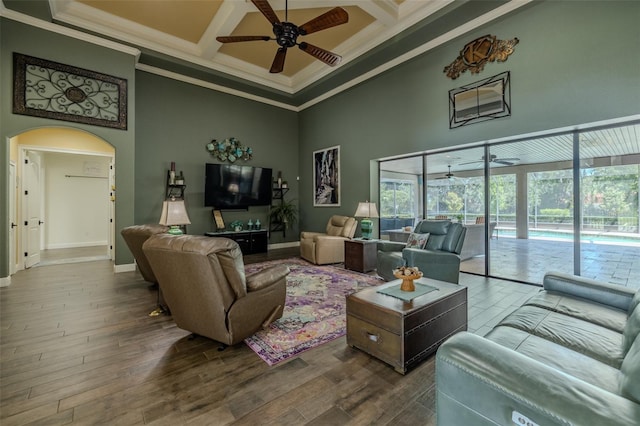 living area with crown molding, ceiling fan, a high ceiling, arched walkways, and coffered ceiling