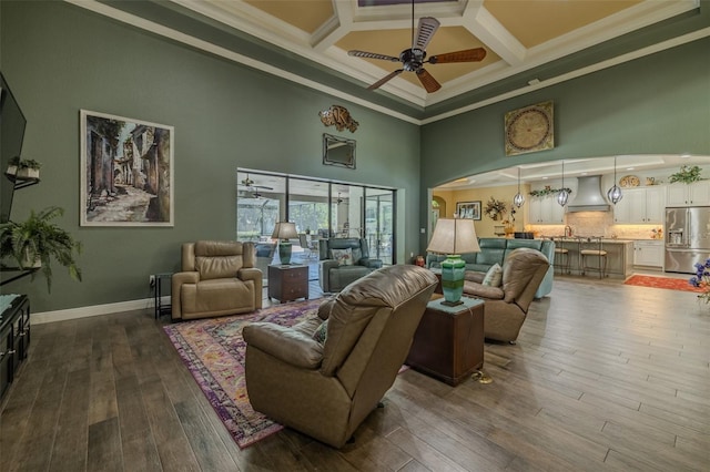 living room with a high ceiling, a ceiling fan, dark wood-type flooring, ornamental molding, and coffered ceiling