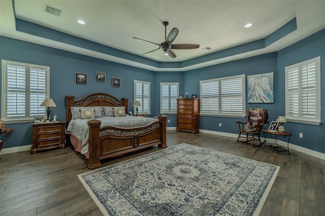 bedroom with a raised ceiling, wood finished floors, and visible vents