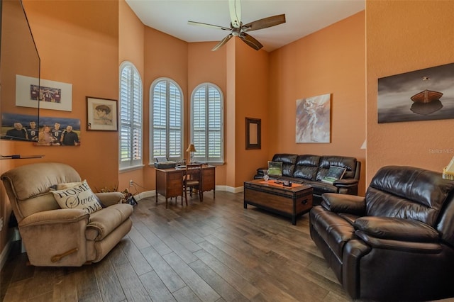 living room with baseboards, ceiling fan, wood finished floors, and a high ceiling