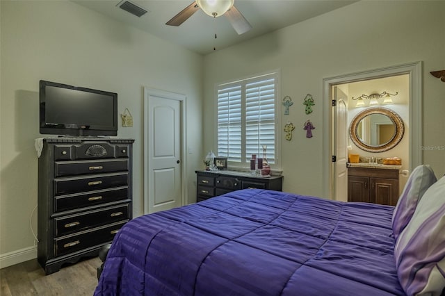 bedroom featuring visible vents, wood finished floors, baseboards, ensuite bathroom, and a sink