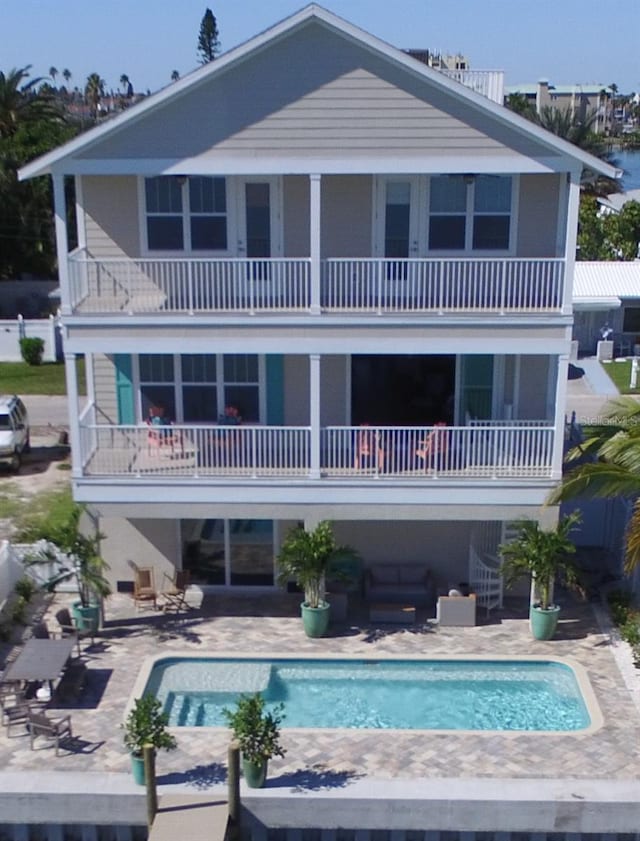 rear view of house with a balcony, a patio area, and an outdoor pool