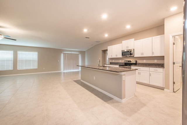 kitchen featuring appliances with stainless steel finishes, a center island with sink, baseboards, open floor plan, and white cabinetry
