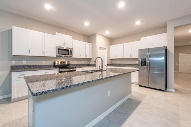 kitchen with appliances with stainless steel finishes, a sink, dark stone countertops, white cabinetry, and a center island with sink