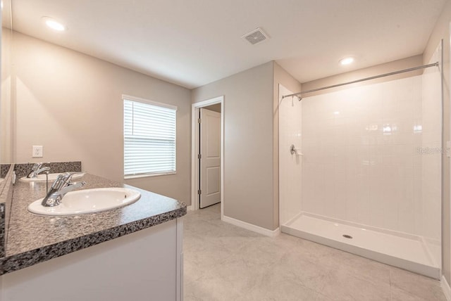 bathroom featuring visible vents, vanity, baseboards, tile patterned floors, and a tile shower