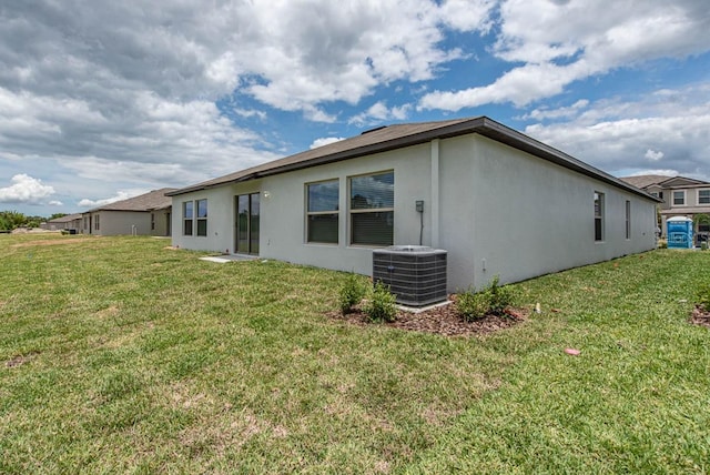 back of house with central AC, stucco siding, and a yard