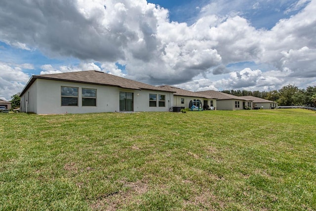 back of property featuring a lawn, central AC unit, and stucco siding