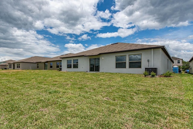 back of property featuring a lawn, central air condition unit, and stucco siding