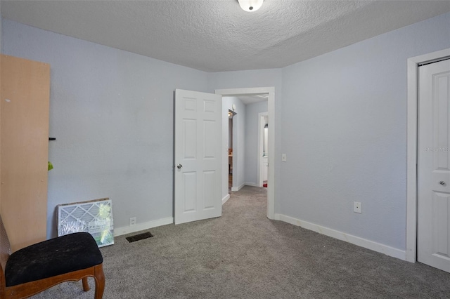 interior space featuring baseboards, carpet flooring, a textured ceiling, and visible vents