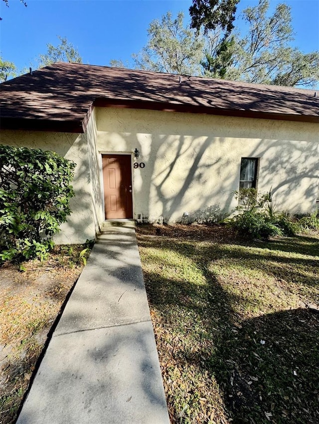 entrance to property featuring roof with shingles and stucco siding