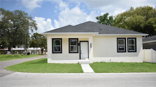 view of front of house with fence, stucco siding, a shingled roof, a front yard, and a porch