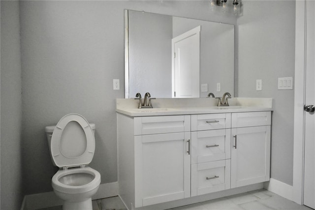 bathroom featuring a sink, toilet, marble finish floor, double vanity, and baseboards