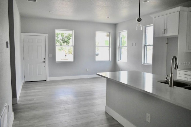 kitchen with a sink, baseboards, white cabinets, and light wood-style floors