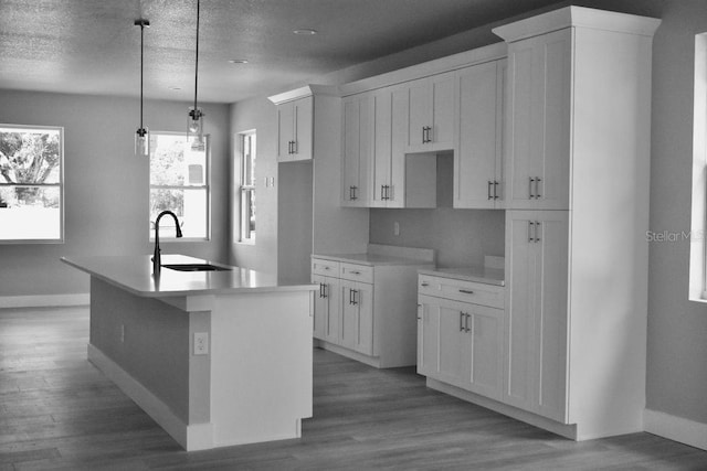 kitchen featuring baseboards, white cabinets, an island with sink, and a sink