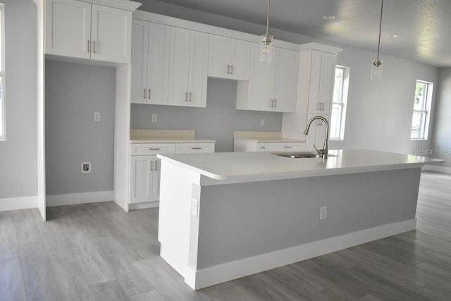 kitchen with white cabinetry, light wood finished floors, an island with sink, and a sink