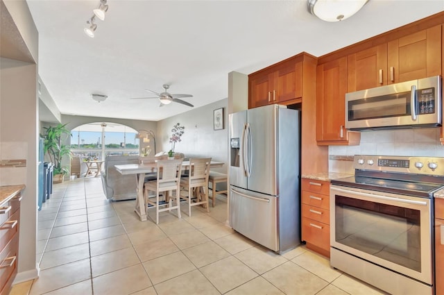 kitchen featuring brown cabinetry, track lighting, ceiling fan, appliances with stainless steel finishes, and light tile patterned floors
