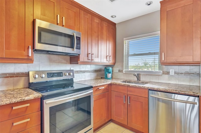 kitchen with light stone counters, a sink, appliances with stainless steel finishes, and brown cabinets