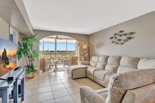 living area featuring light tile patterned floors, arched walkways, and a ceiling fan