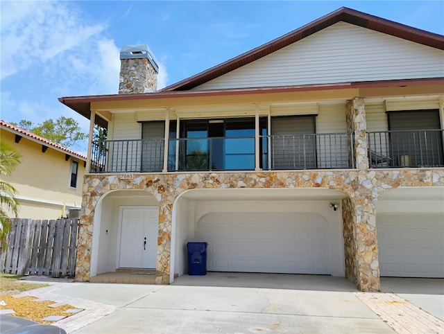 7085 Sunset Dr S Unit A, Saint Petersburg, FL 33707 - view of front facade with a balcony, an attached garage, stone siding, a chimney, and concrete driveway