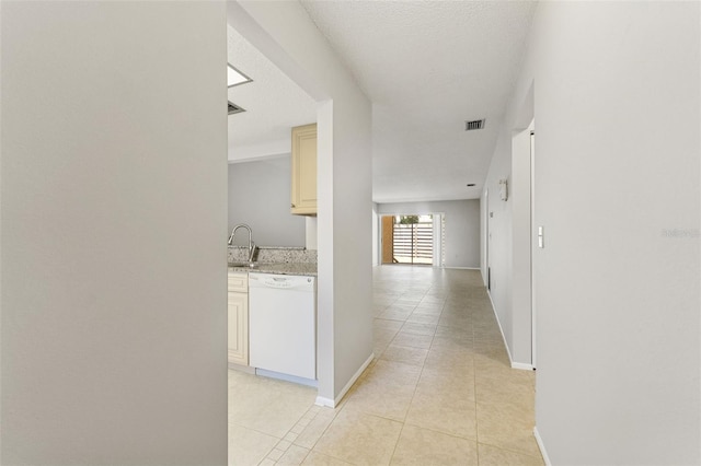 hallway featuring visible vents, a sink, baseboards, and light tile patterned floors