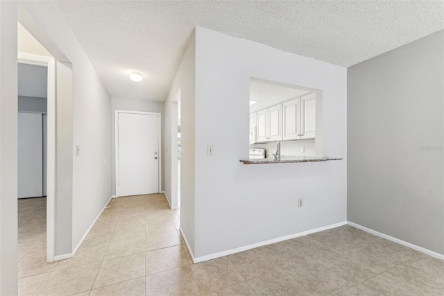hall with baseboards, a textured ceiling, and light tile patterned floors