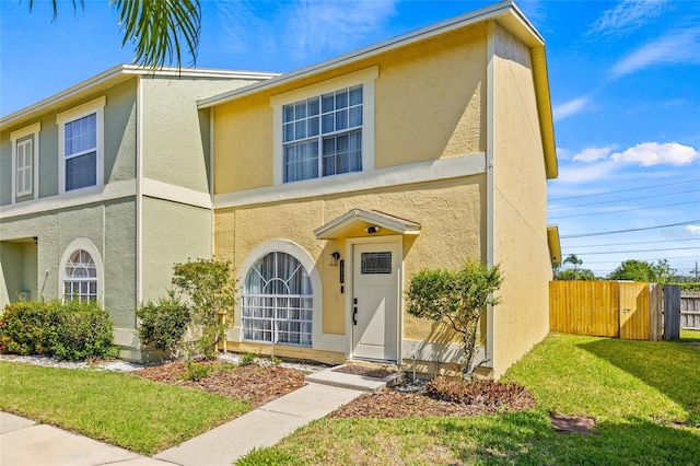 traditional home featuring a front lawn, stucco siding, and fence