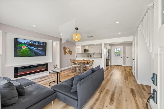 living room with visible vents, baseboards, a glass covered fireplace, recessed lighting, and light wood-style flooring