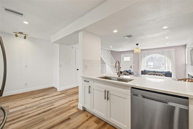 kitchen with stainless steel dishwasher, a sink, visible vents, and light wood-type flooring