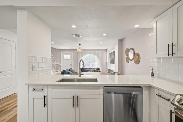 kitchen featuring a sink, a peninsula, open floor plan, stainless steel appliances, and white cabinetry