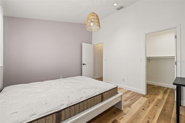 bedroom featuring visible vents, baseboards, light wood finished floors, a spacious closet, and a high ceiling