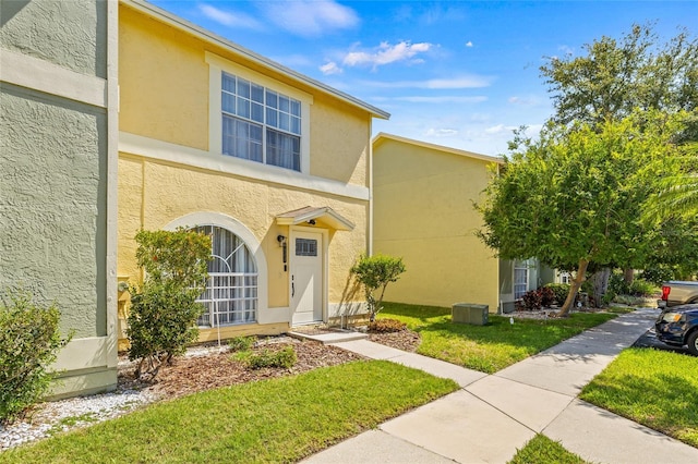 traditional home featuring cooling unit, a front lawn, and stucco siding