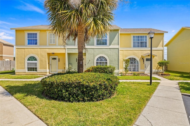 view of front of house featuring fence, stucco siding, and a front yard
