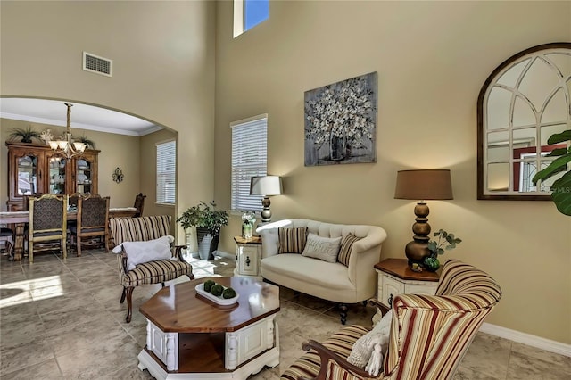 living area with visible vents, arched walkways, ornamental molding, an inviting chandelier, and a high ceiling